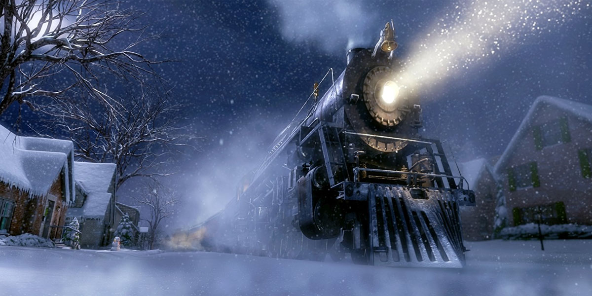 A old-fashioned steam engine train sits in the center of a neighborhood on a snowy night. The train's single headlight shines into the dark night.