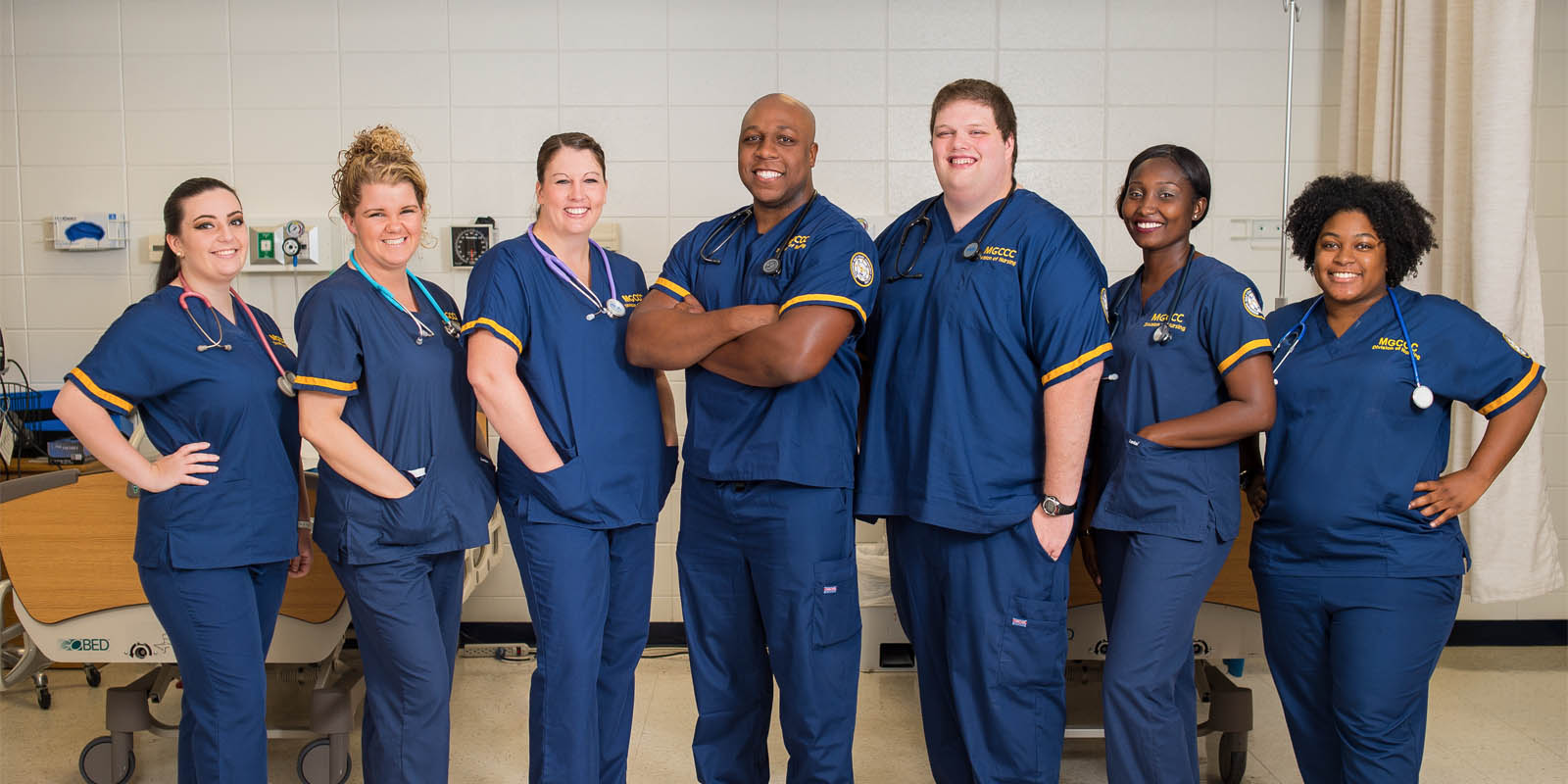 Seven students from the ADN nursing program dressed in their clinical uniforms stand in the skills lab.