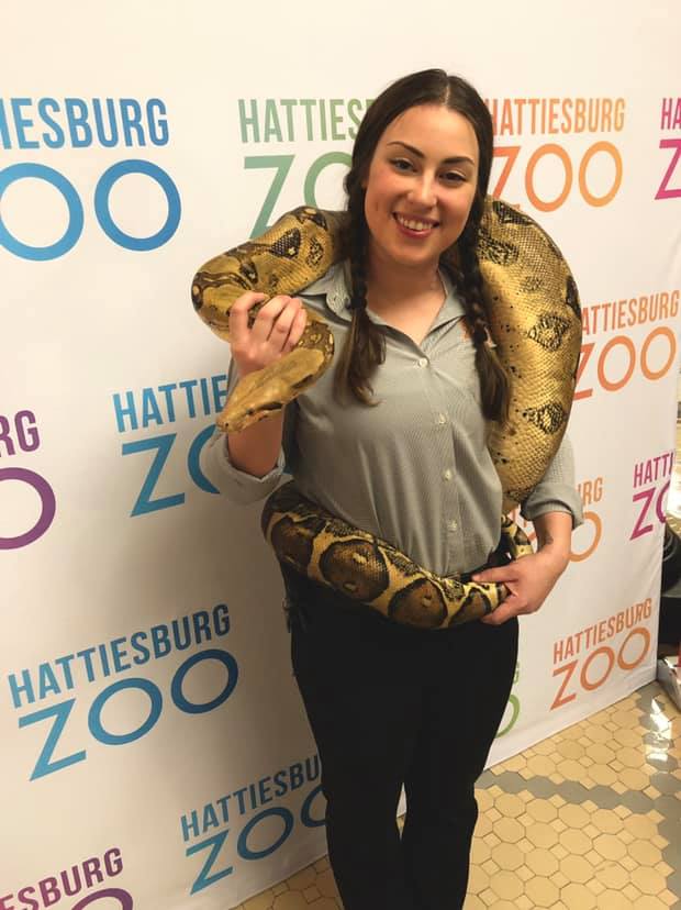 Laura Leggett stands in front of a Hattiesburg Zoo sign with a boa constrictor draped over her shoulders