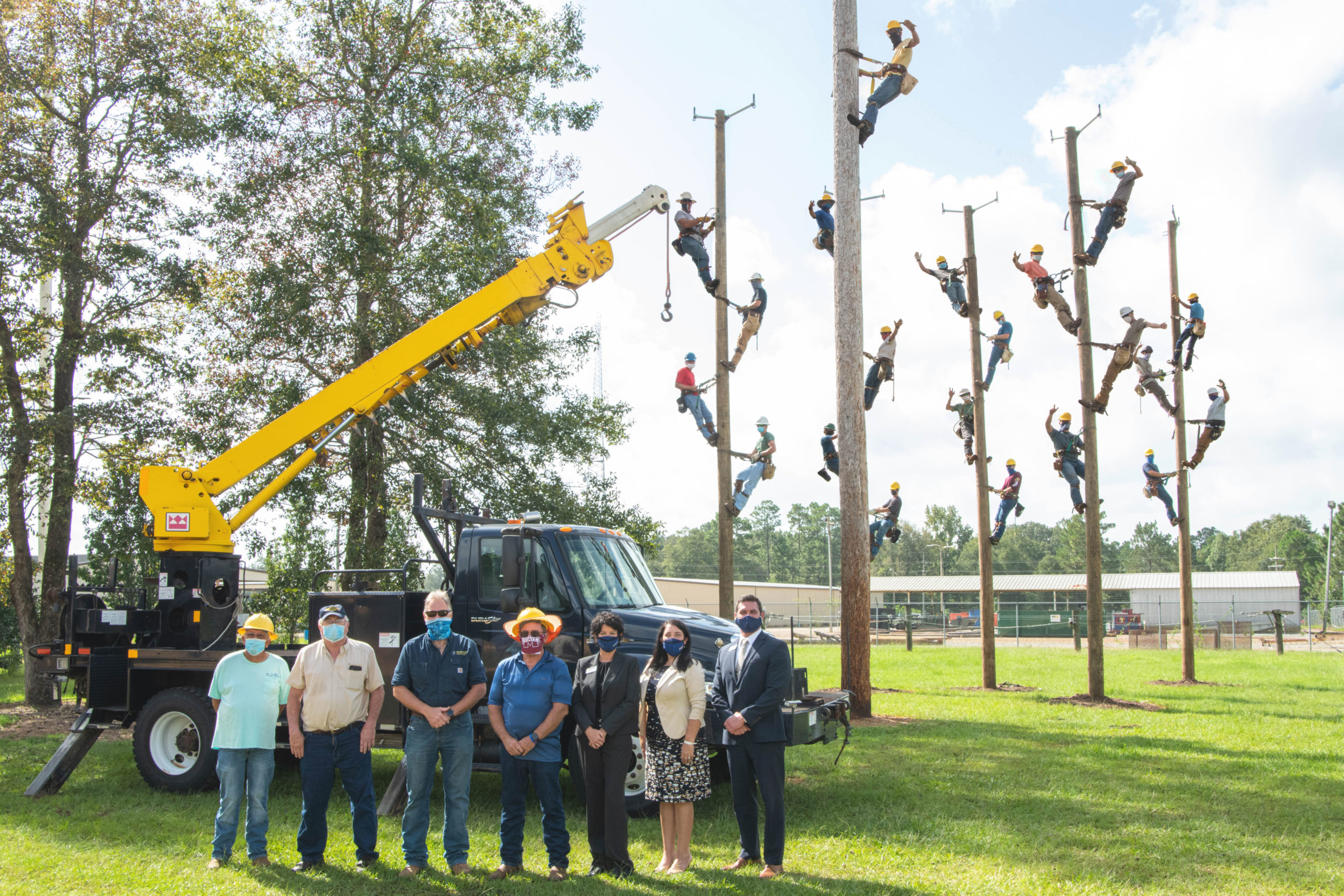 Photo: From left in the forefront are H.L. Ivey, MGCCC Electric Lineman instructor; Jerry Pittman, Pearl River Valley Electric Power Association mechanic; Raymond May, Safety coordinator/manager of Automotive Services for Pearl River Valley Electric Power Association; David Eubanks, MGCCC Electric Lineman instructor; Dr. Lisa Rhodes, administrative dean at the George County Center; Dr. Kady Pietz, associate vice president of Foundation and Alumni Relations; and Dr. Ladd Taylor, vice president of the Perkinston Campus and George County Center. In the background, on poles, are students in the Apprentice Electric Lineman program at MGCCC’s George County Center.