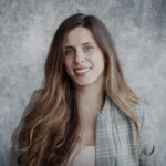 Nikoletta Ranno standing in front of a gray background smiling.