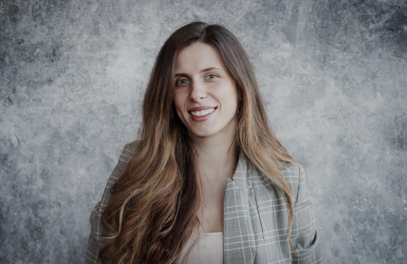 Nikoletta Ranno standing in front of a gray background smiling.