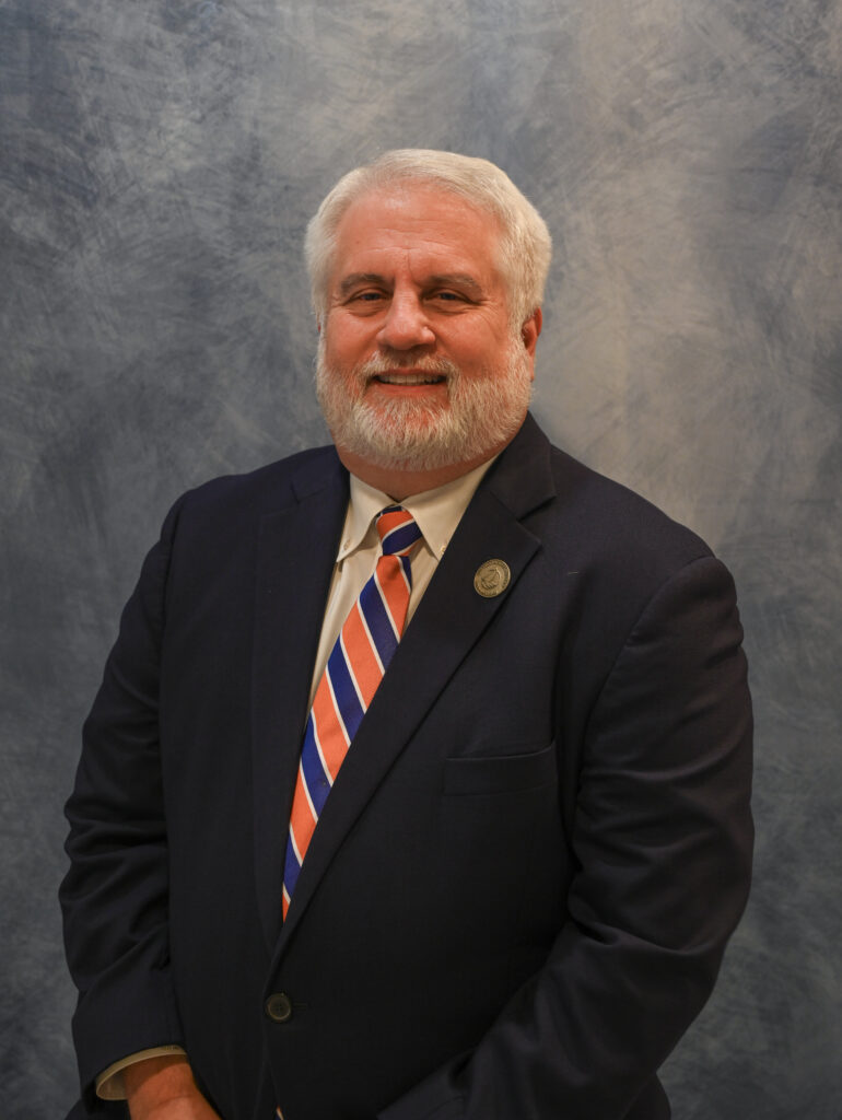Glen East portrait with stripped red/blue tie and navy blue jacket.
