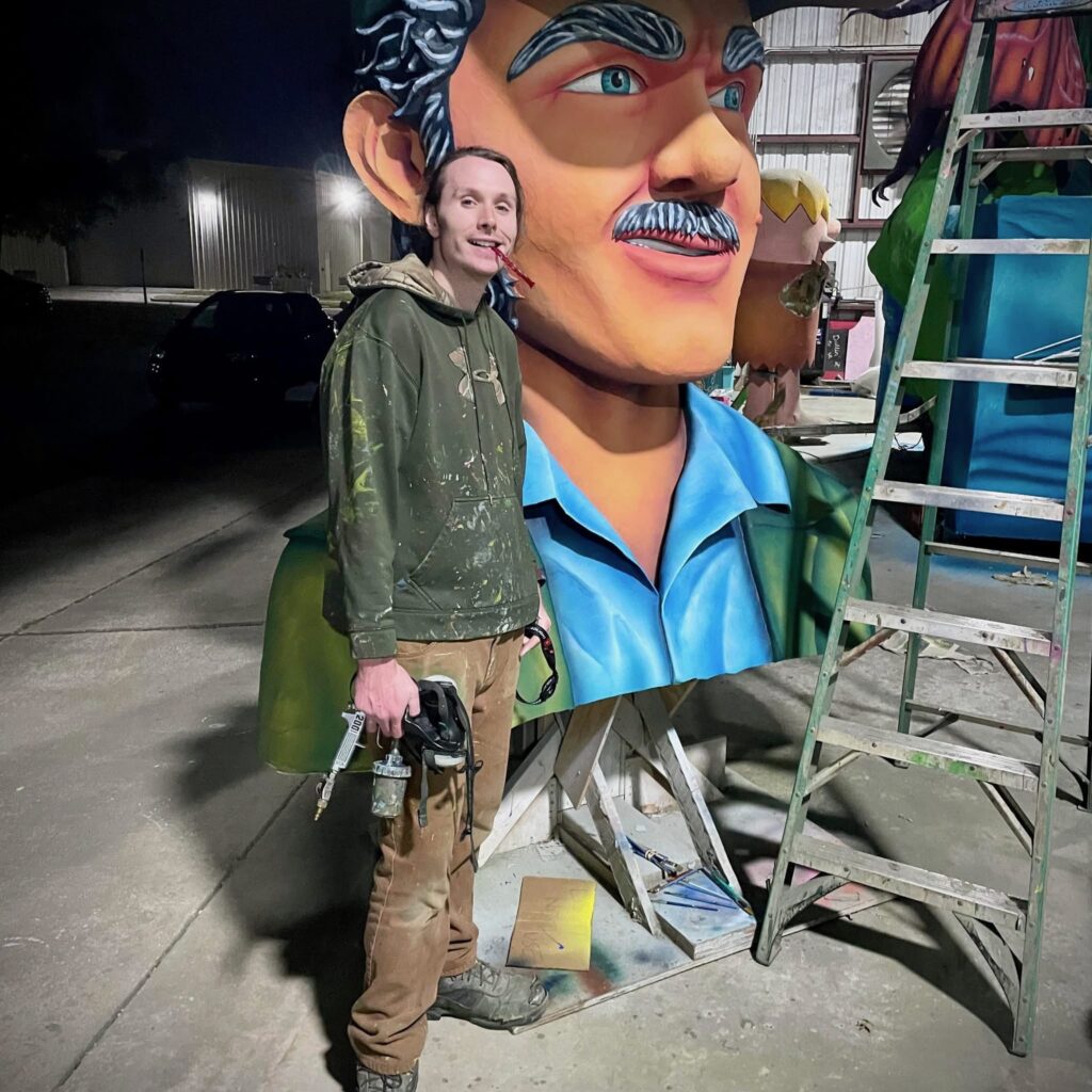 Jackson Jones standing in front of a Mardi Gras float figurehead with a paint spray gun.