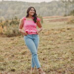 Rubi Ramirez standing in a field with a pink shirt and blue jeans.